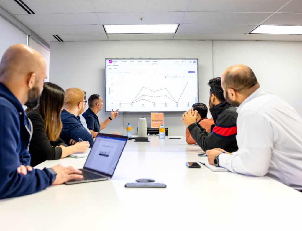Next Step TSP Managed IT Services Team Meeting. Colleagues reviewing performance graphs on a large digital screen.