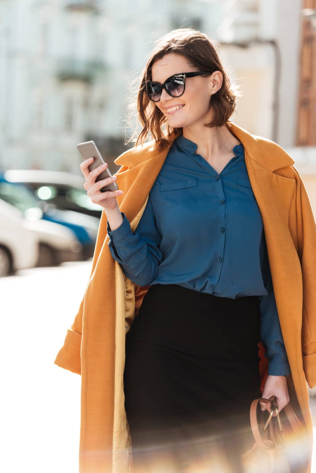 smiling young woman in sunglasses and coat looking at her new NSTSP Phone Bill on her mobile phone.
